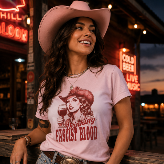 Cowgirl wearing the Drinking Fascist Blood light pink T-shirt outside a neon western saloon