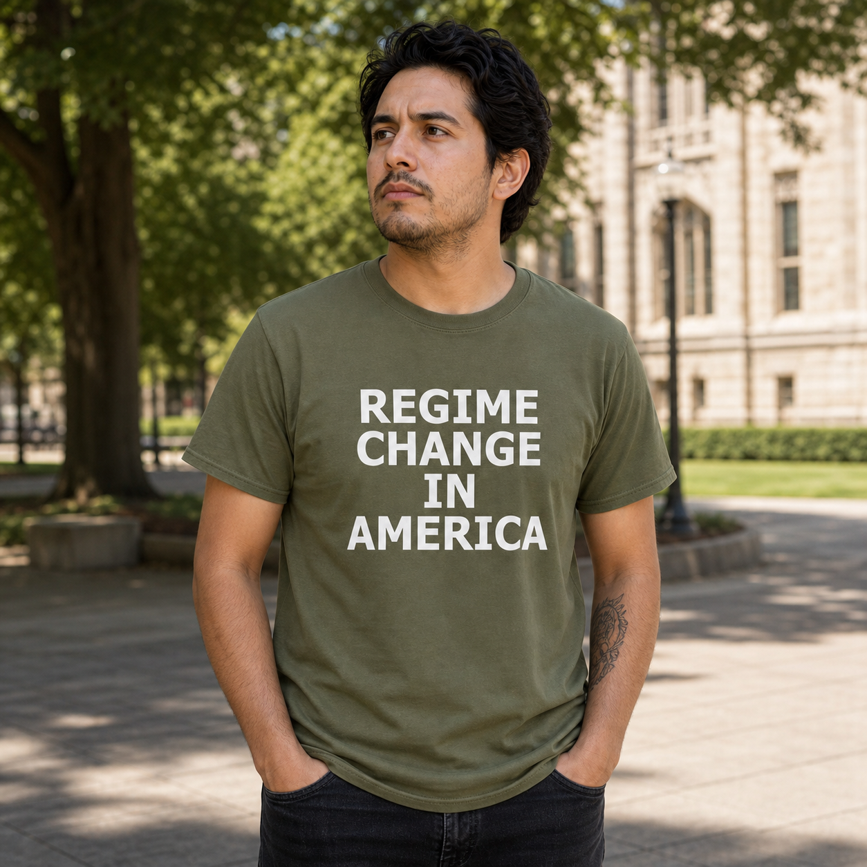 Man wearing the Regime Change in America olive T-shirt on a campus civic walkway